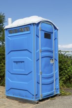 Blue and white portable chemical toilet temporarily installed by the roadside for public use in