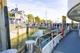 View from the ferry deck to the shore with waiting passengers and autumn foliage, Meersburg, Lake