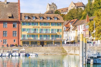 Hotel building with colourful facades on the shore and docked boats in sunny weather, Meersburg,