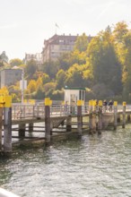 Wooden jetty on the lakeshore with autumnal trees and promenade, Mainau Island, Lake Constance,