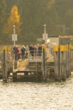 People waiting at a jetty surrounded by trees with autumn colours, Mainau Island, Lake Constance,