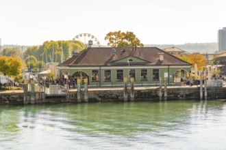 A building at the harbour with autumnal vegetation and a Ferris wheel in the background in a