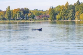 A boat sails across a calm lake surrounded by autumn trees, Constance, Lake Constance, Germany