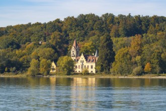 A picturesque castle on the shore of a lake surrounded by autumnal trees with a clear sky,