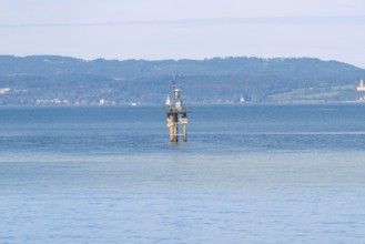 A tower stands in the calm waters of a large lake with green hills and a clear sky in the