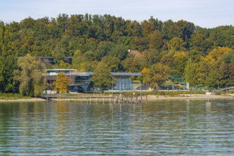 Modern building on the shore of a lake, surrounded by autumnal trees and a pier, Constance, Lake