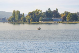 Small boat on a lake with autumn trees on the shore under a clear sky, Constance, Lake Constance,