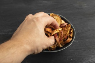 Dried Apples in ceramic bowl with hand on black wooden background. Side view, close up. healthy