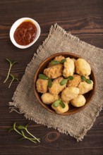 Fried crispy Chicken Nuggets with ketchup, microgreen on brown wooden background and linen textile.