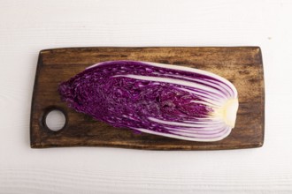 Purple Chinese cabbage on cutting board on white wooden background, top view, flat lay, close up,