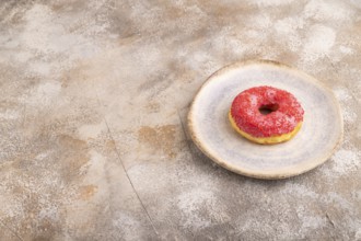Pink Donut with sprinkles on blue ceramic plate on brown concrete background, side view, copy