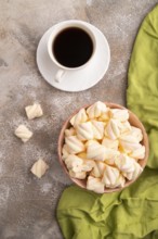 Orange and pink marshmallow in ceramic bowl on brown concrete background and green textile, top