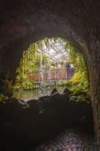 View from a cave, waterfall and people on a bridge, surrounded by lush plants, Mainau Island, Lake