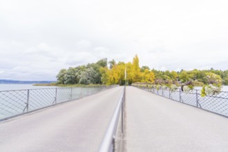 Long bridge over the water, flanked by autumn-coloured trees in shades of yellow and green, Mainau