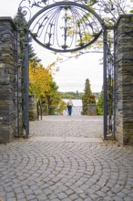 View through an ornate iron gate onto a cobbled driveway and a view beyond, Mainau Island, Lake