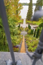 View through a gate onto a well-kept garden path leading to the lake, surrounded by autumn trees,