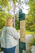Woman standing in front of a signpost in autumn forest, Mainau flower island, Lake Constance,