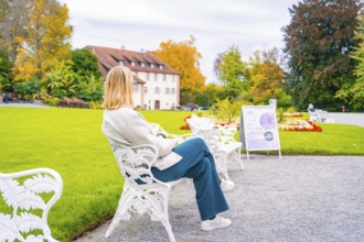 Woman sitting on a white garden bench, in the colourful autumn garden, Mainau flower island, Lake