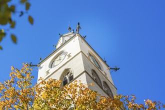 A church tower with a clock, surrounded by autumn leaves in front of a clear blue sky, Überlingen,