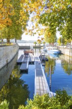A jetty on the water in a small harbour, with autumnal trees on the shore, Überlingen, Lake