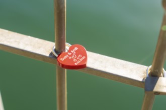 Red heart lock with engraving on the railing over green water, Überlingen, Lake Constance, Germany