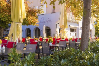 Cosy outdoor area of a café with red and black chairs, tables and large parasols in autumn light,