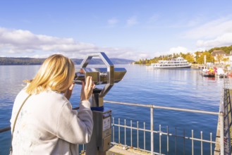 A woman looks through a telescope at a lake with ships and a clear autumn sky, Überlingen, Lake