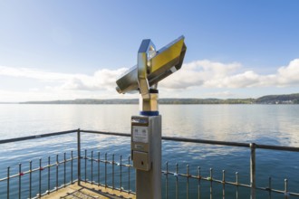 Binoculars on the shore pointing to a peaceful lake with blue sky and clouds, Überlingen, Lake