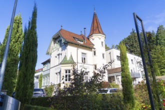 Historic building with tower and pointed roofs, surrounded by trees under a clear sky, Überlingen,