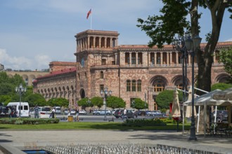 An impressive historic stone building with colonnades, surrounded by people and cars in an urban