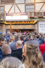 Crowds of people standing in front of the entrance to a wooden building, expectant atmosphere,