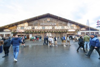 Visitors move in front of a large wooden building, lively atmosphere, Cannstatter Wasen folk