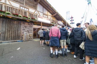 People standing in a row in front of a traditional wooden building, waiting for admission,