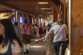 People in traditional dress walk through a corridor in a venue, Cannstatter Wasen folk festival,