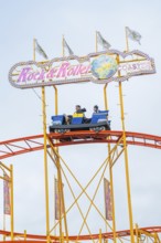 Roller coaster car on rails with rock and roller lettering and colourful flags, Cannstatter Wasen