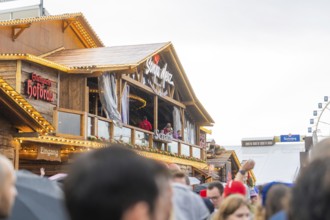 Bavarian wooden building in rainy weather with people in the foreground, Cannstatter Wasen folk