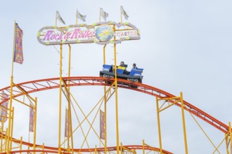Colourful roller coaster with brave passengers on the rails in the amusement park, Cannstatter