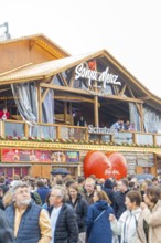 People on a balcony of a wooden building with a big heart in the foreground, Cannstatter Wasen folk
