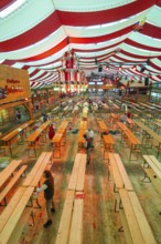 Setting up a marquee with red and white stripes, empty benches and light-coloured wooden floor,