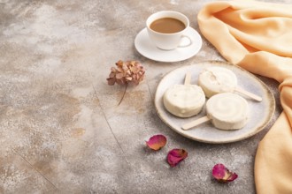 ?hocolate Ice cream in white glaze, cup of coffee, on brown concrete background and orange textile,