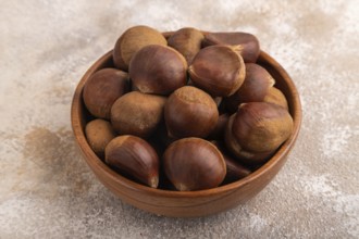 Wooden bowl with raw edible ?hestnuts on brown concrete background, side view, close up, minimalism