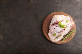 Raw Turkey Thigh with spices and rosemary on cutting board on black concrete background. top view,