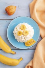 White ?ottage cheese, Curd, with Banana on blue wooden background and orange textile, top view,