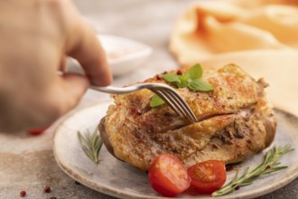 Fried Turkey Thigh with spices and rosemary on plate with hand on brown concrete background and