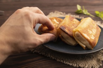 Fried crispy pancakes with meat and cheese with hand on brown wooden background and linen textile.