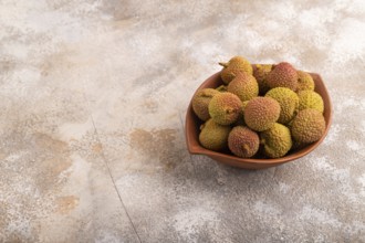 Ripe Lychee on clay bowl on brown concrete background, side view, copy space, minimalism