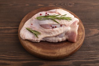 Raw Turkey Thigh with spices and rosemary on cutting board on brown wooden background. side view,