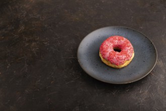 Pink Donut with sprinkles on blue ceramic plate on black concrete background, side view, copy