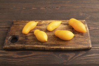 Yellow tomatoes on cutting board on brown wooden background. Side view, copy space. healthy food,