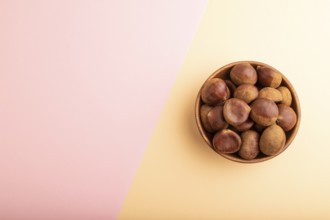 Wooden bowl with raw edible ?hestnuts on pink and orange paper pastel background, top view, flat